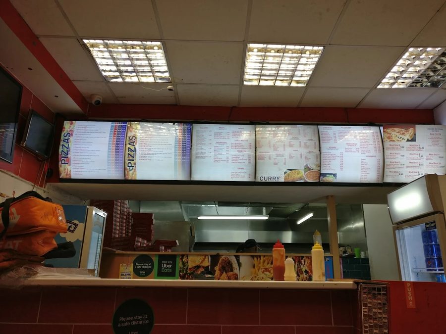 Illuminated menu boards inside Adils Takeaway showing pizzas, curries and kebabs